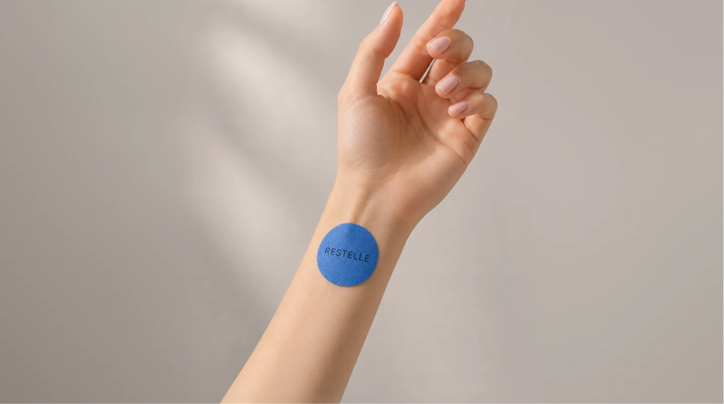 A person's arm with a blue, circular patch on the wrist that reads 'RESTELL'.