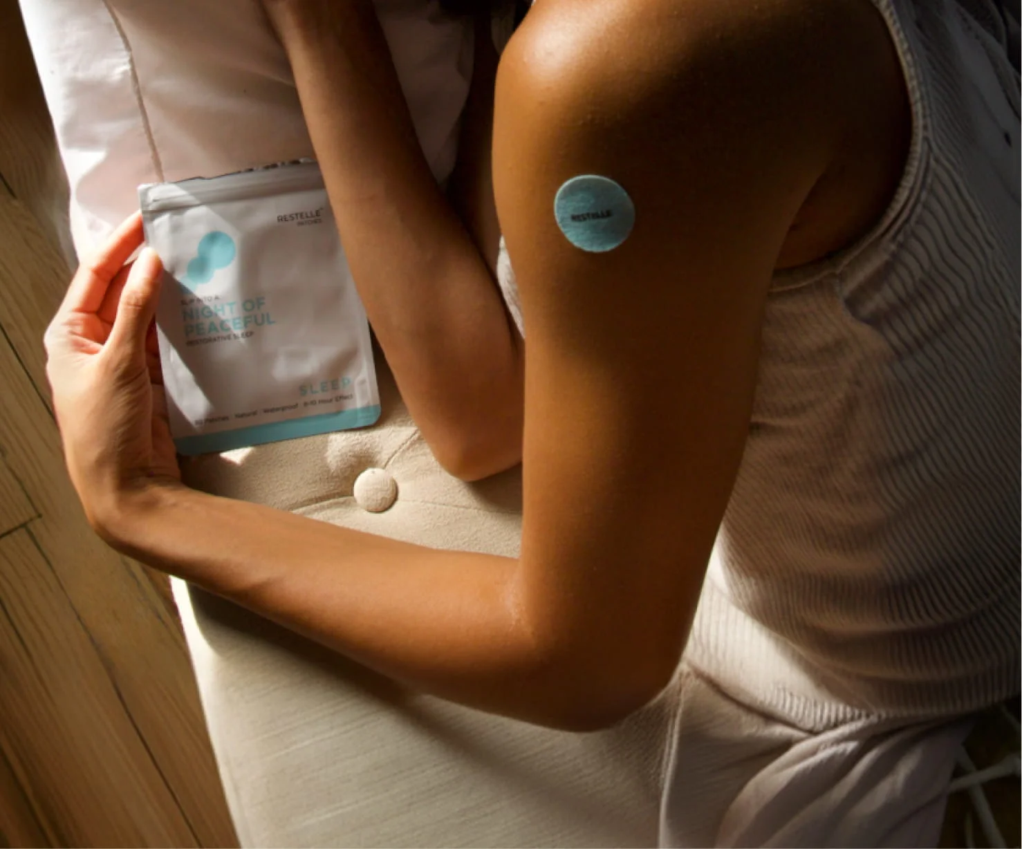 A woman with a sleep patch on her arm lies down holding the product packaging.