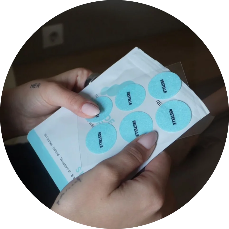 A person's hands holding a sheet of light blue, circular patches with the word 'RESTELLE' printed on them.