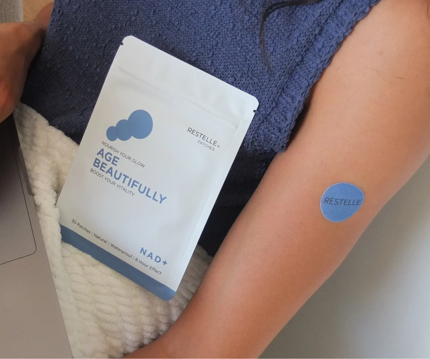 A person wearing a blue Restelle patch on their arm next to the product packaging.