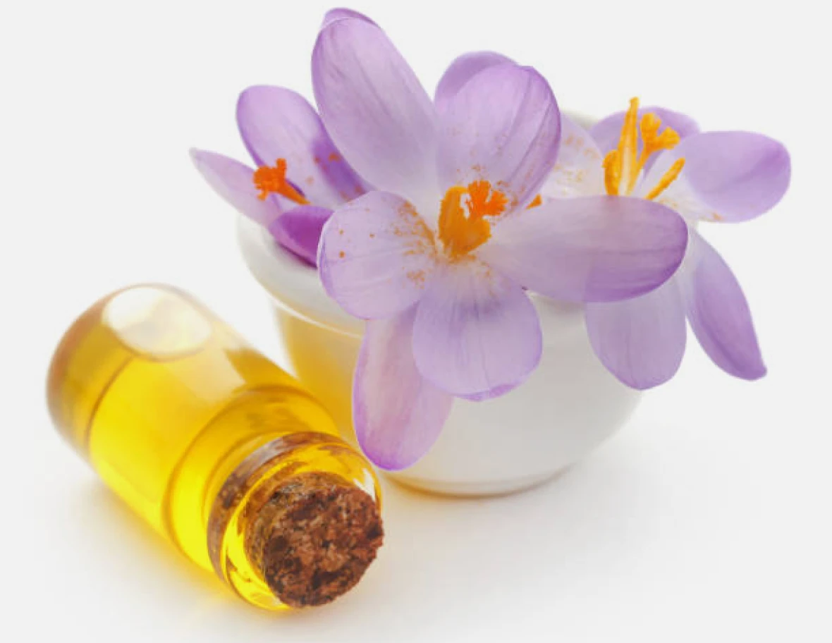 Purple flowers beside a small vial of yellow oil.