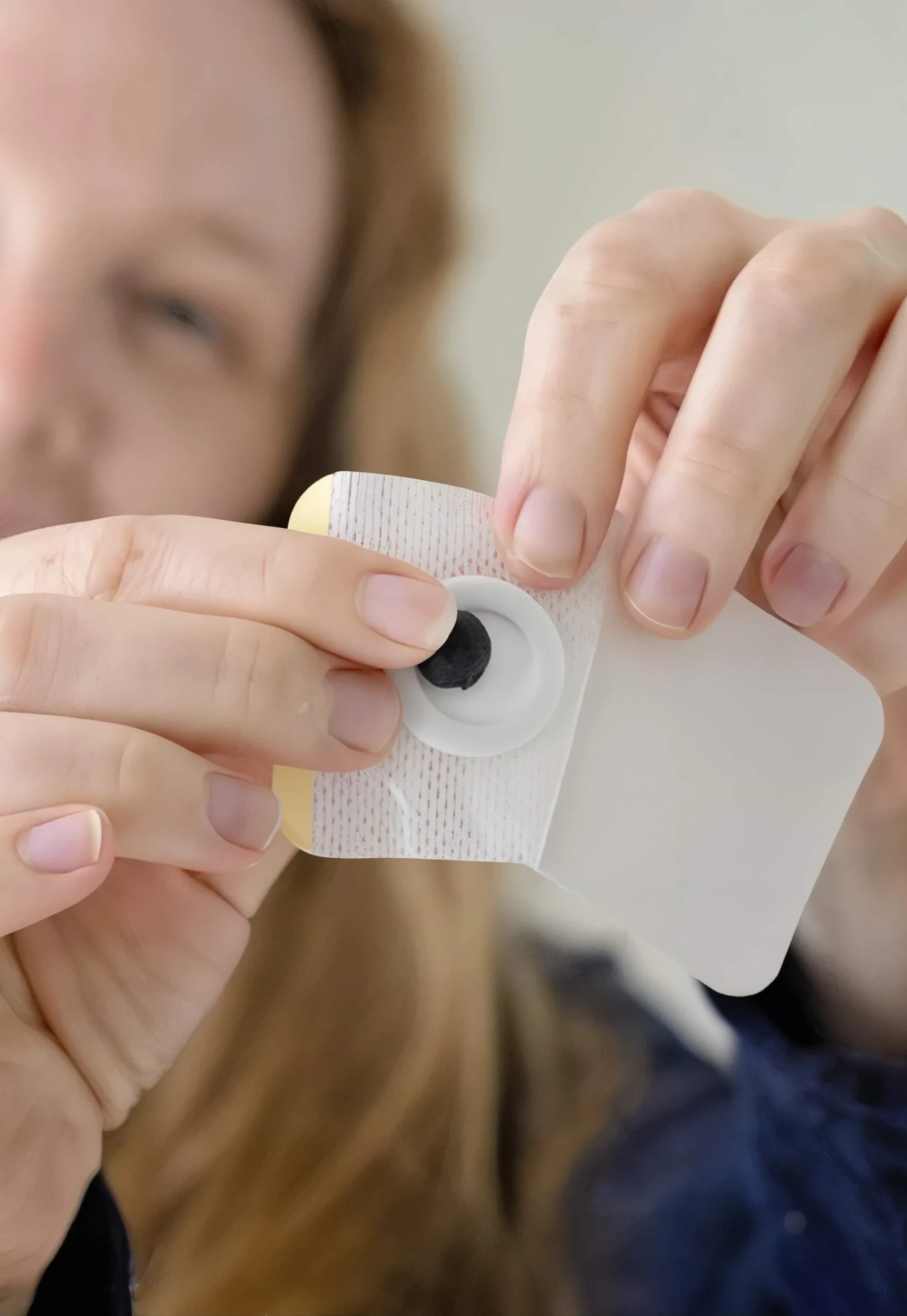 Person holding a medical adhesive patch with a black circular component.