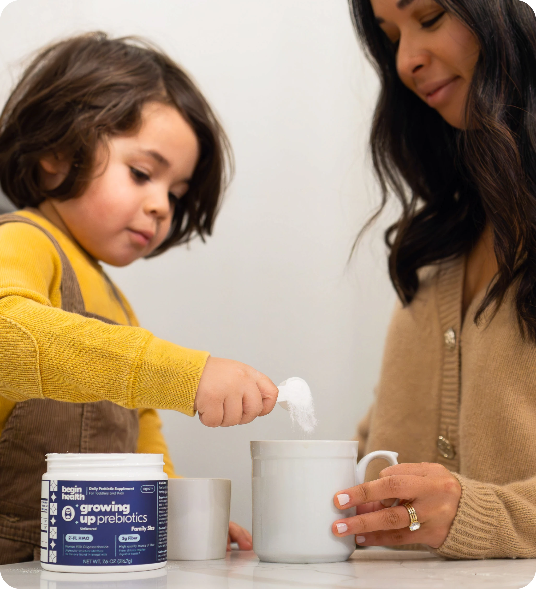Child adding powder to a mug with an adult's assistance.