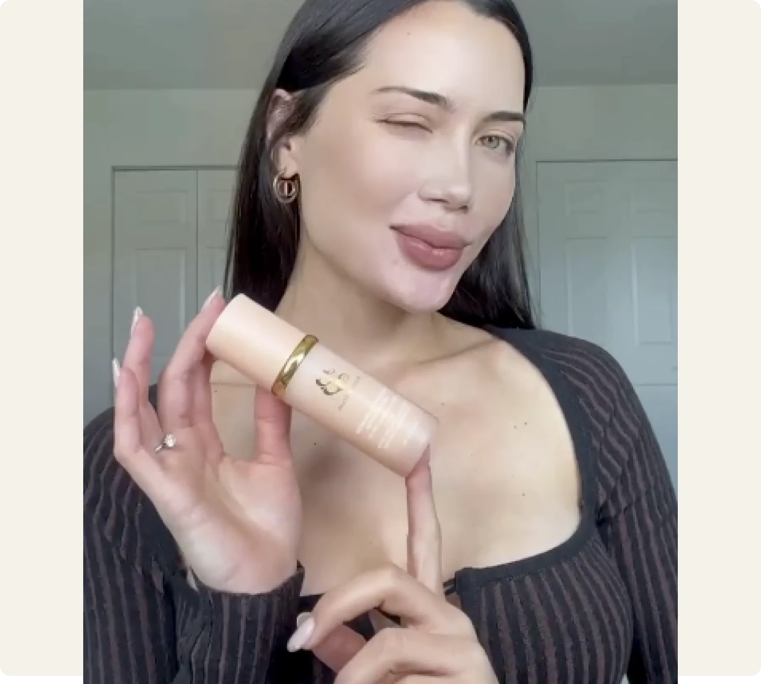 Person winking, holding a skincare product bottle.