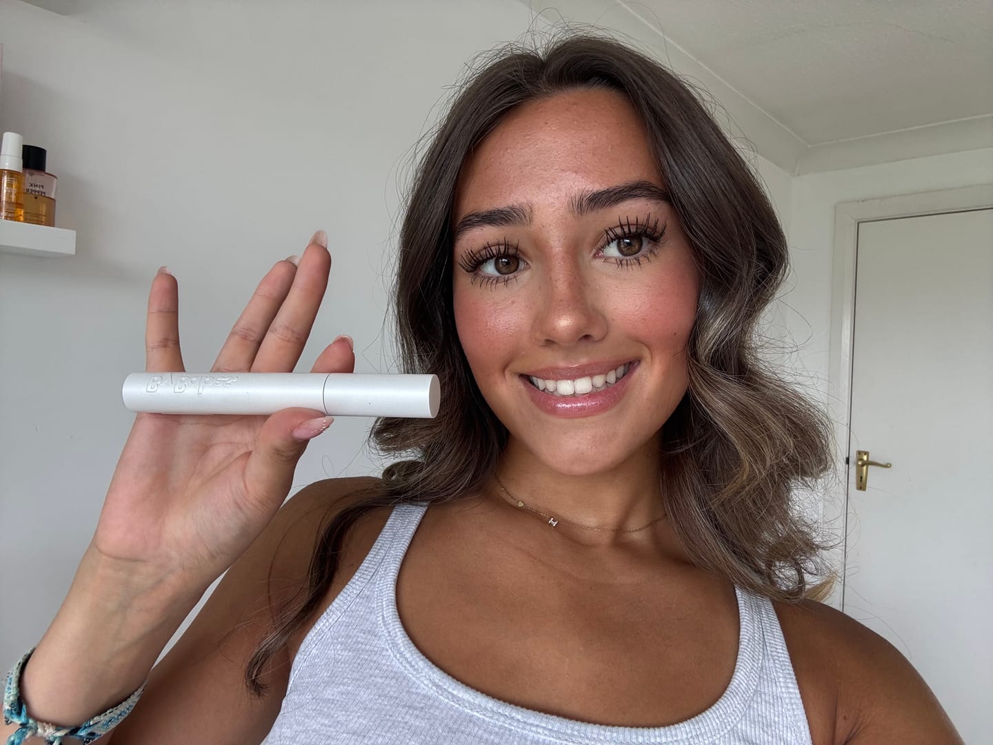 Person smiling and holding a white cylindrical object in a room.