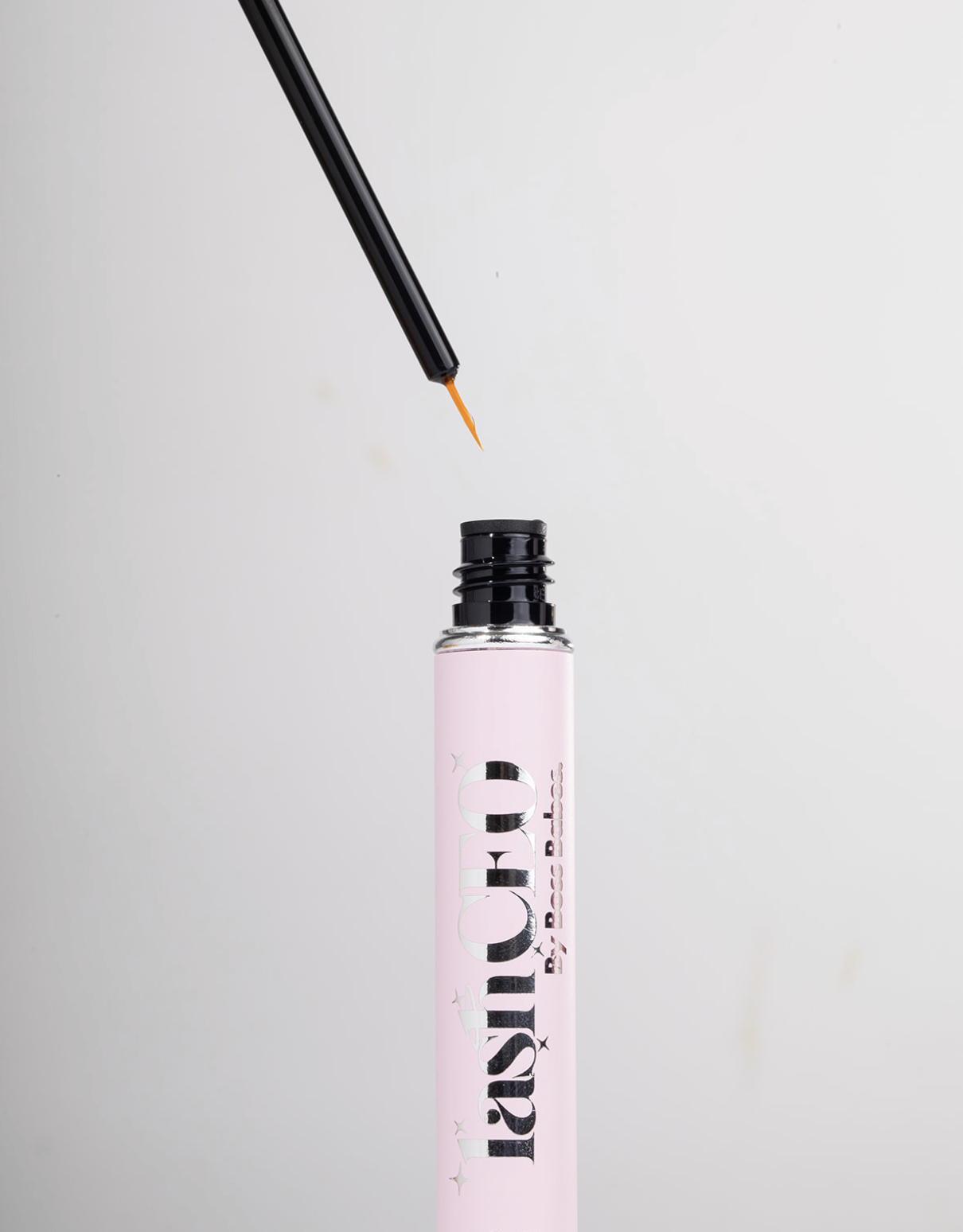 Pink mascara tube with black applicator and orange tip on a gray background.