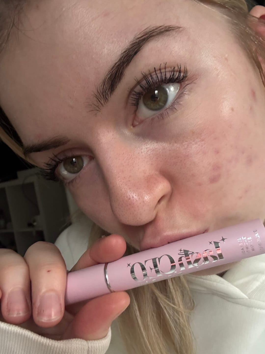 Person holding a pink mascara tube close to their face.