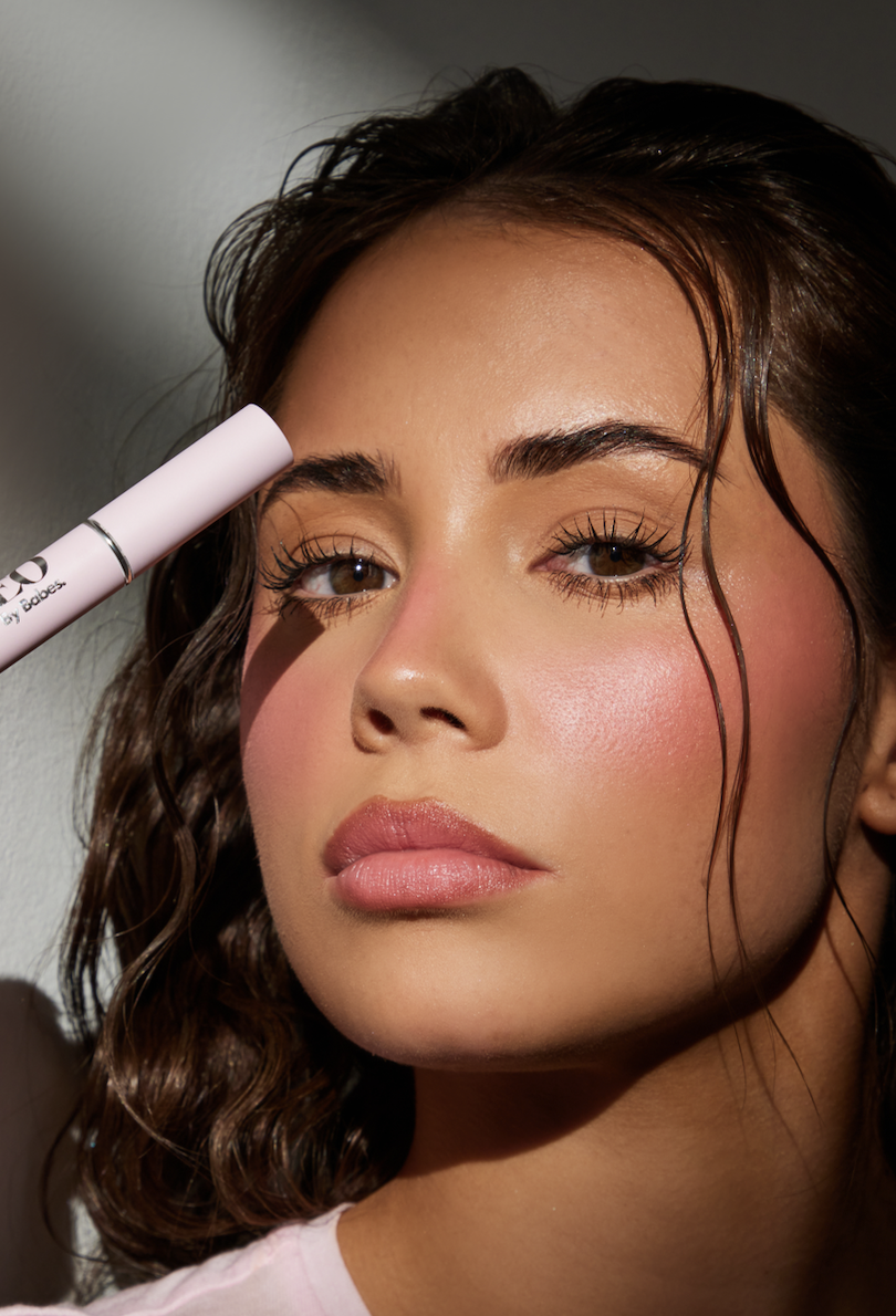 Woman with natural makeup holding a makeup product near her face.