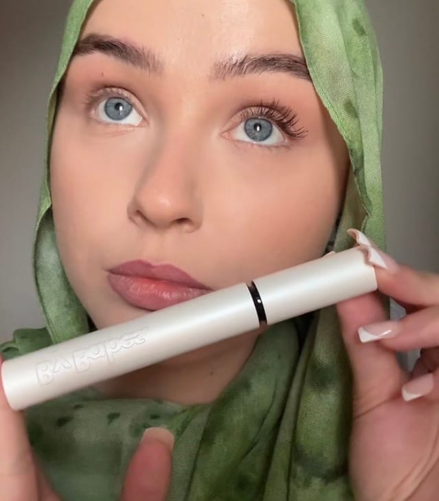 Person in green hijab holding a white mascara tube.