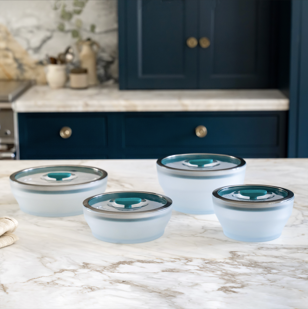 Four frosted glass containers with lids on a marble countertop.