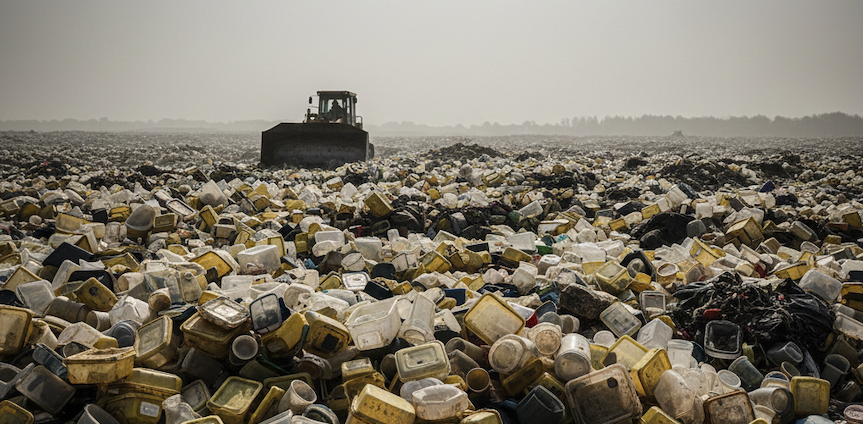 Bulldozer amidst a vast landfill of plastic containers and waste.
