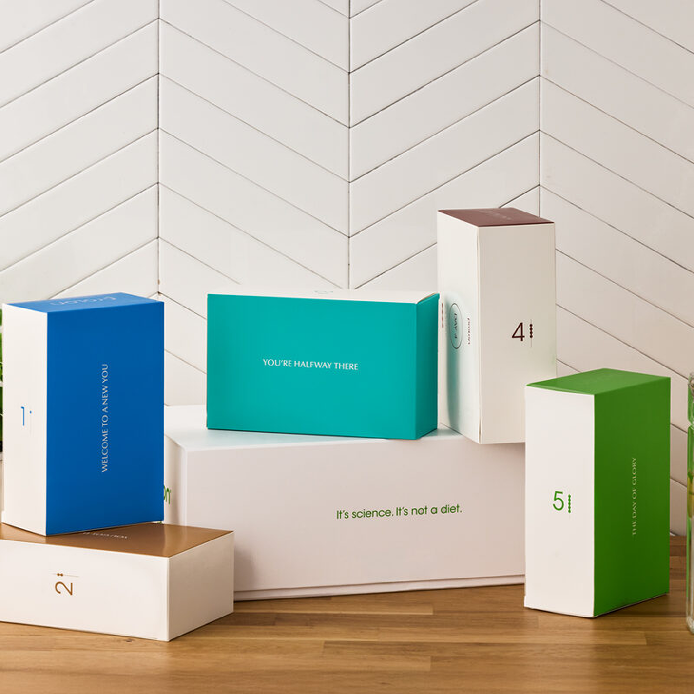 A collection of colorful numbered product boxes arranged on a wooden surface against a white tiled wall.