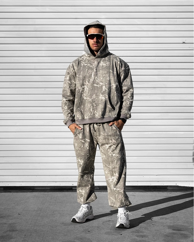 Person in camo hoodie and pants, wearing sunglasses, standing against a white garage door.