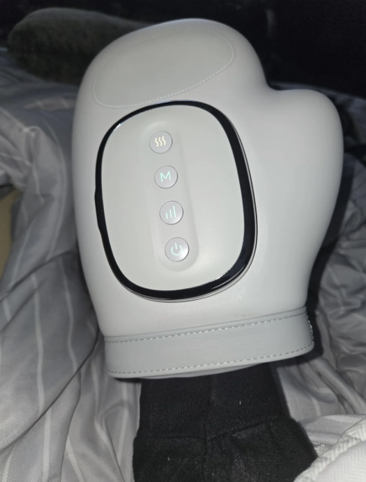 A white electronic massage glove with control buttons on a striped fabric surface.