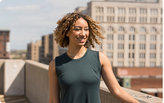 Person smiling outdoors with city buildings in the background.