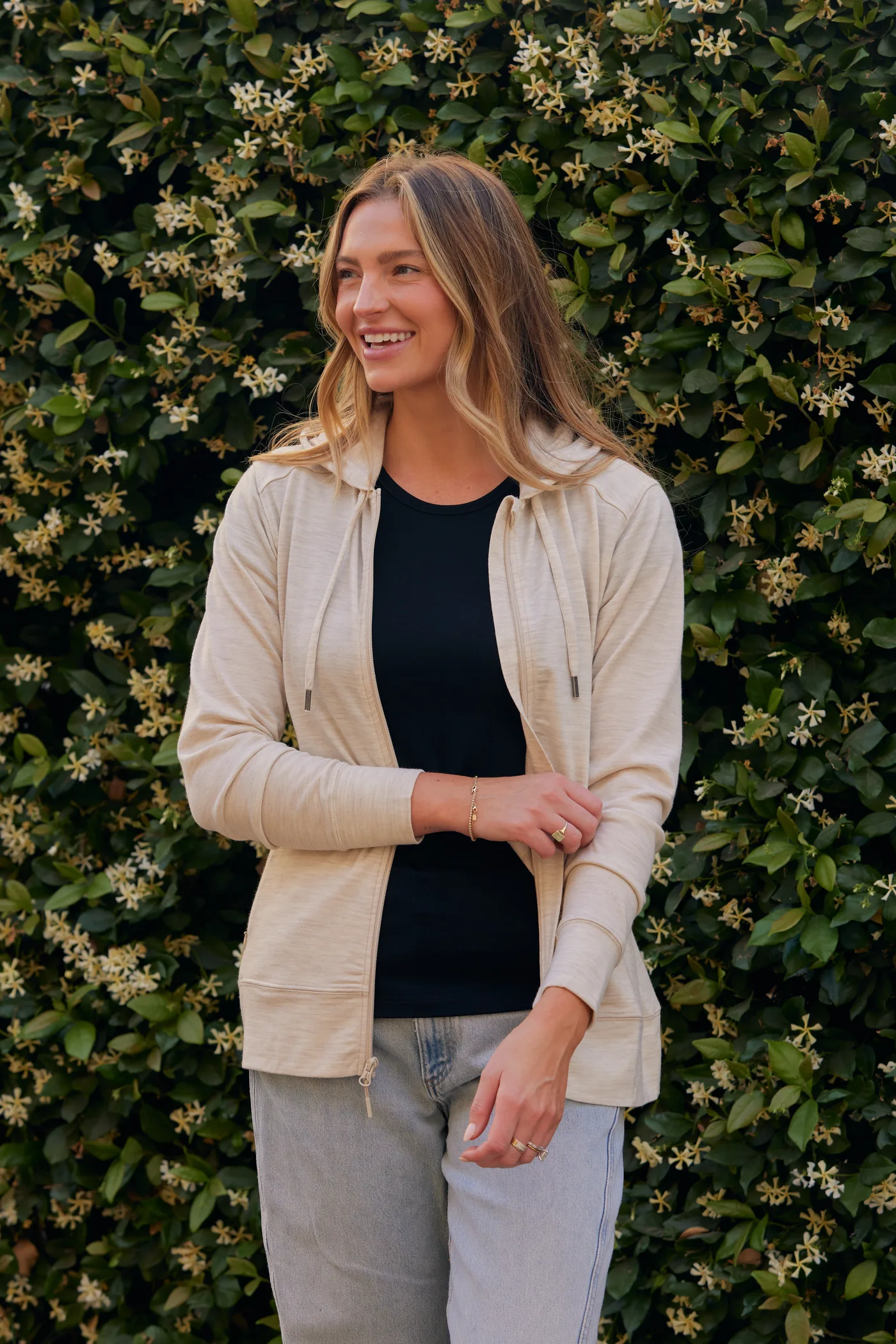 Woman wearing a cream Ryann Merino Hoodie in front of flowering greenery