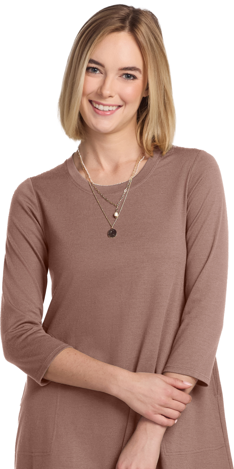 Smiling person with short blonde hair wearing a brown top and layered necklaces.