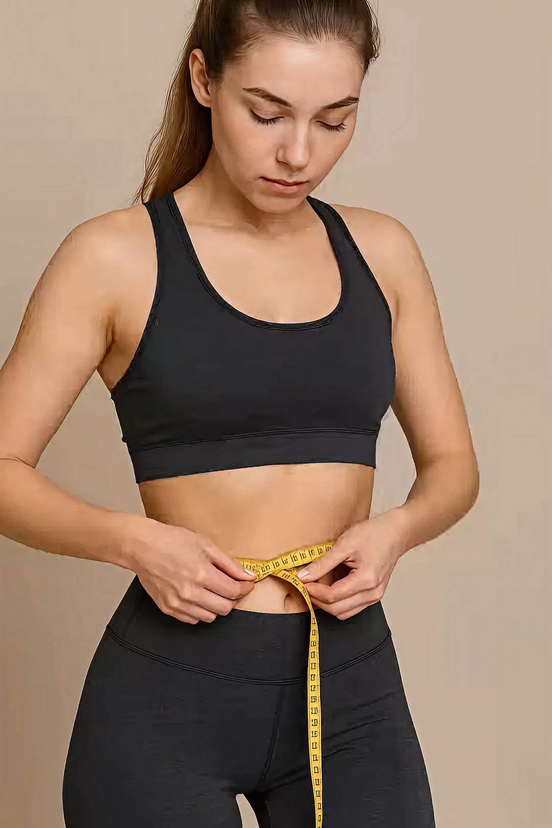 Woman measuring waist with yellow tape in activewear.