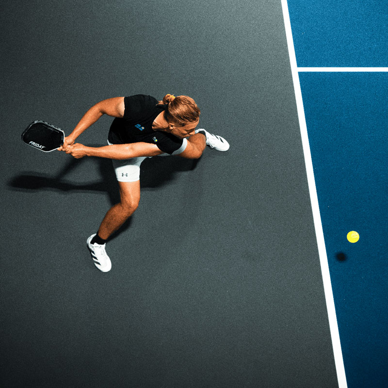 A person plays pickleball, swinging a paddle at a ball on a blue court.
