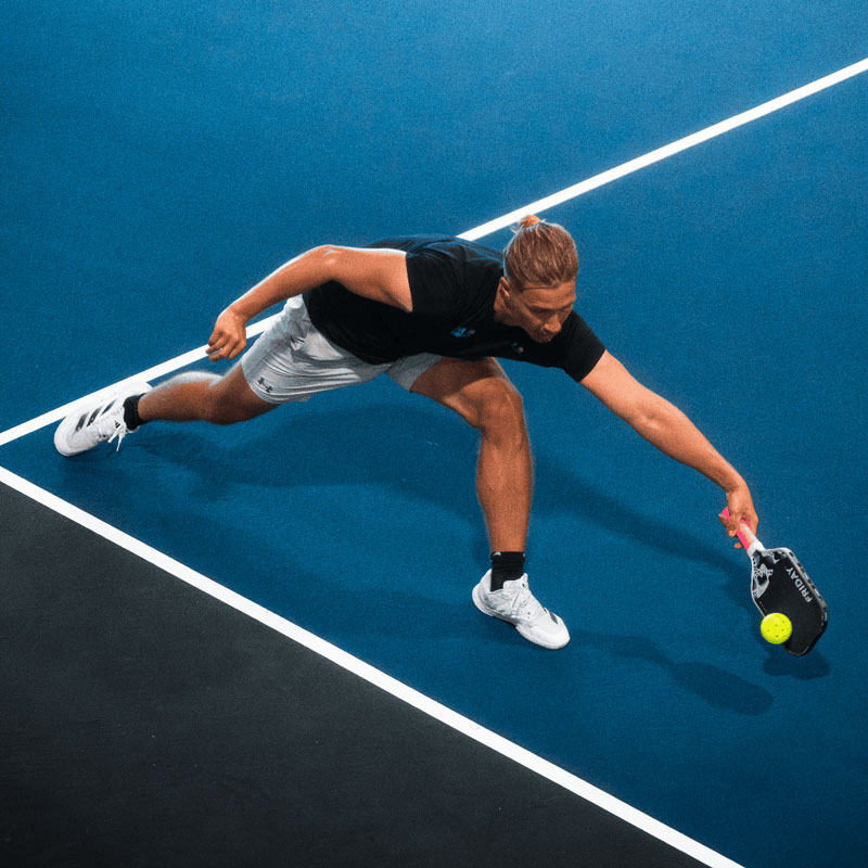Person playing padel on a blue court, reaching for the ball with a paddle.