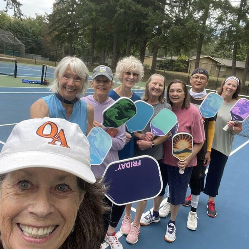 Group of people holding pickleball paddles on a court.