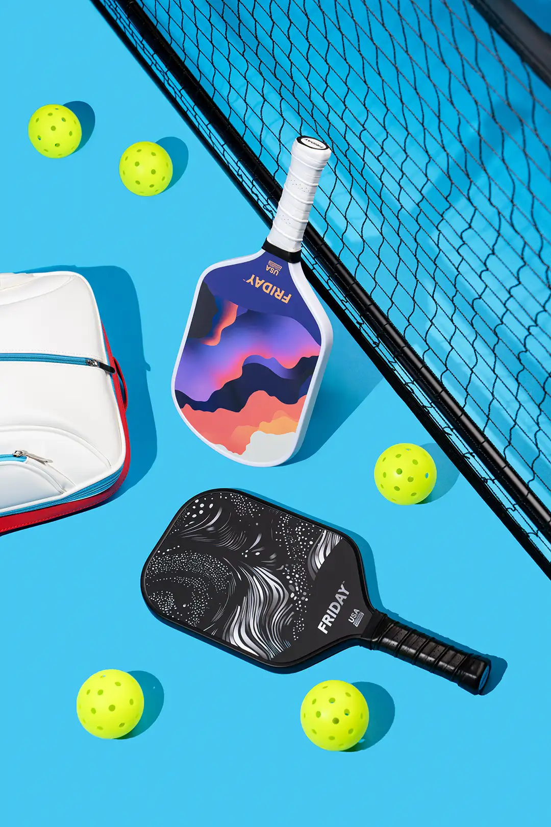 Colorful pickleball paddles and balls on a blue court next to a net.