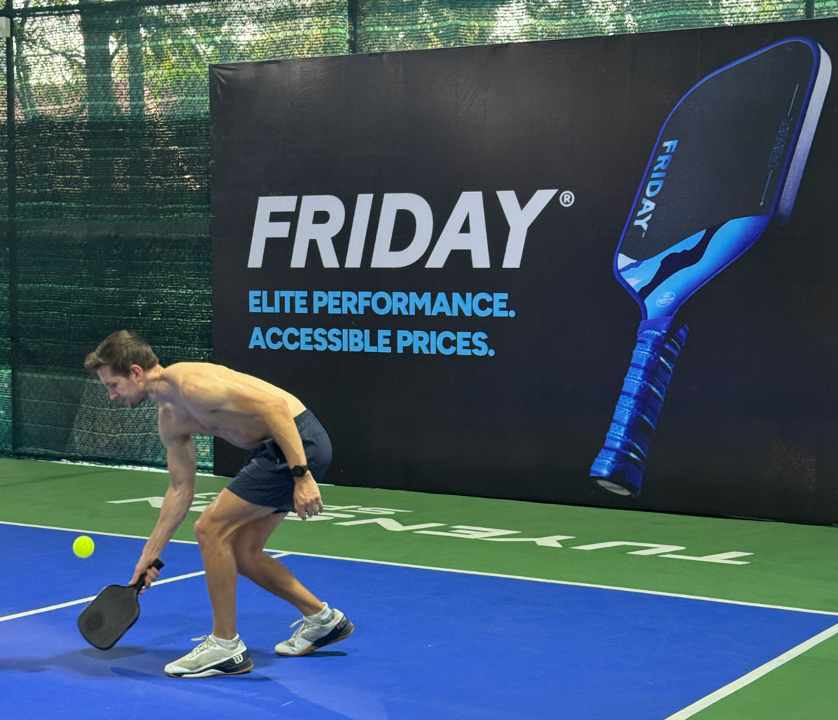 Man playing pickleball on a court with a large advertisement in the background.