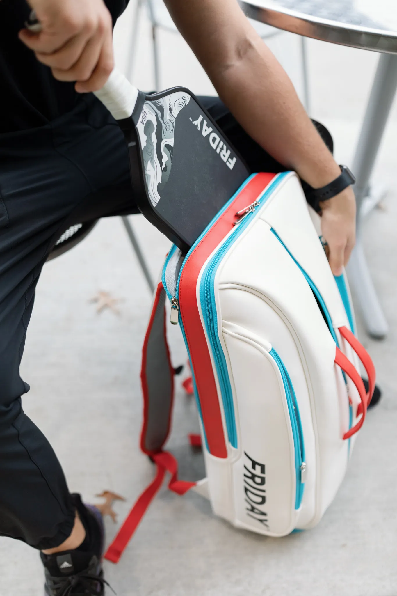Person placing a paddle into a white sports bag labeled 'FRIDAY.'