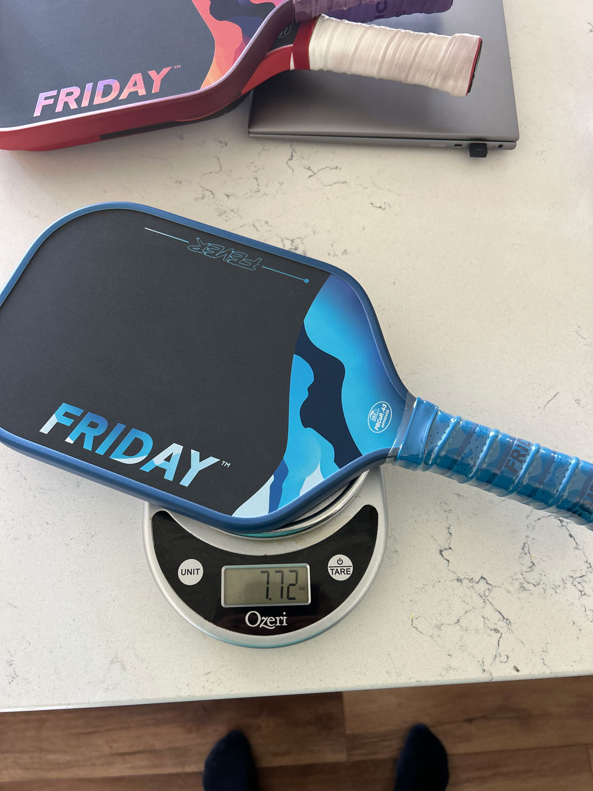 Blue pickleball paddle on a digital scale showing 7.72 ounces.