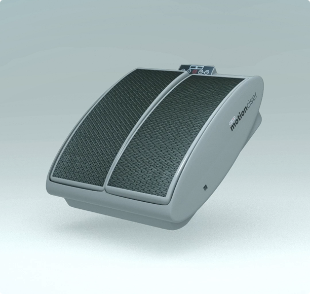 A grey Motionciser leg exerciser machine with two textured black footplates and a small digital display.