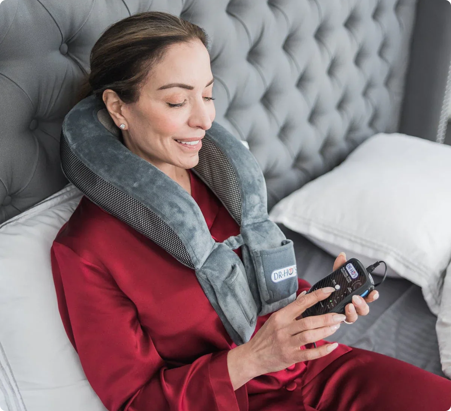 Woman in red robe using a neck massager on a bed.