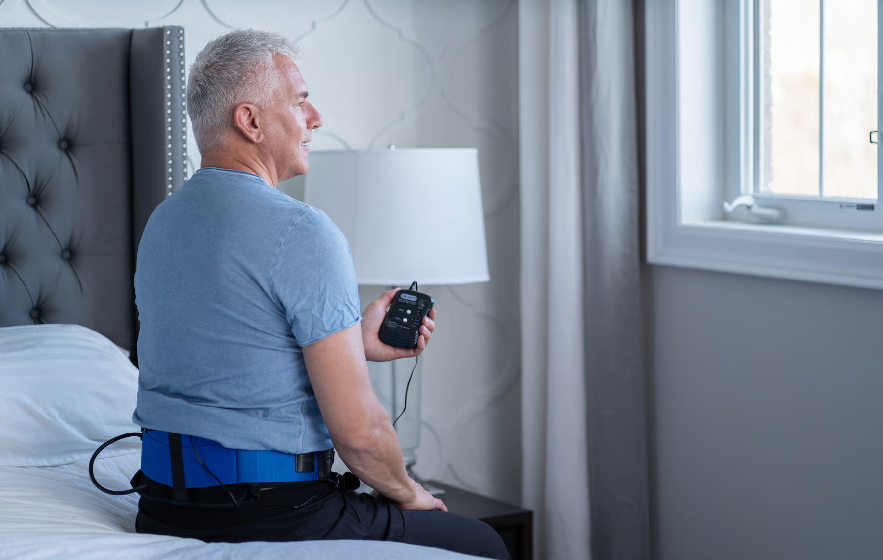 Person sitting on a bed using a device with wires.