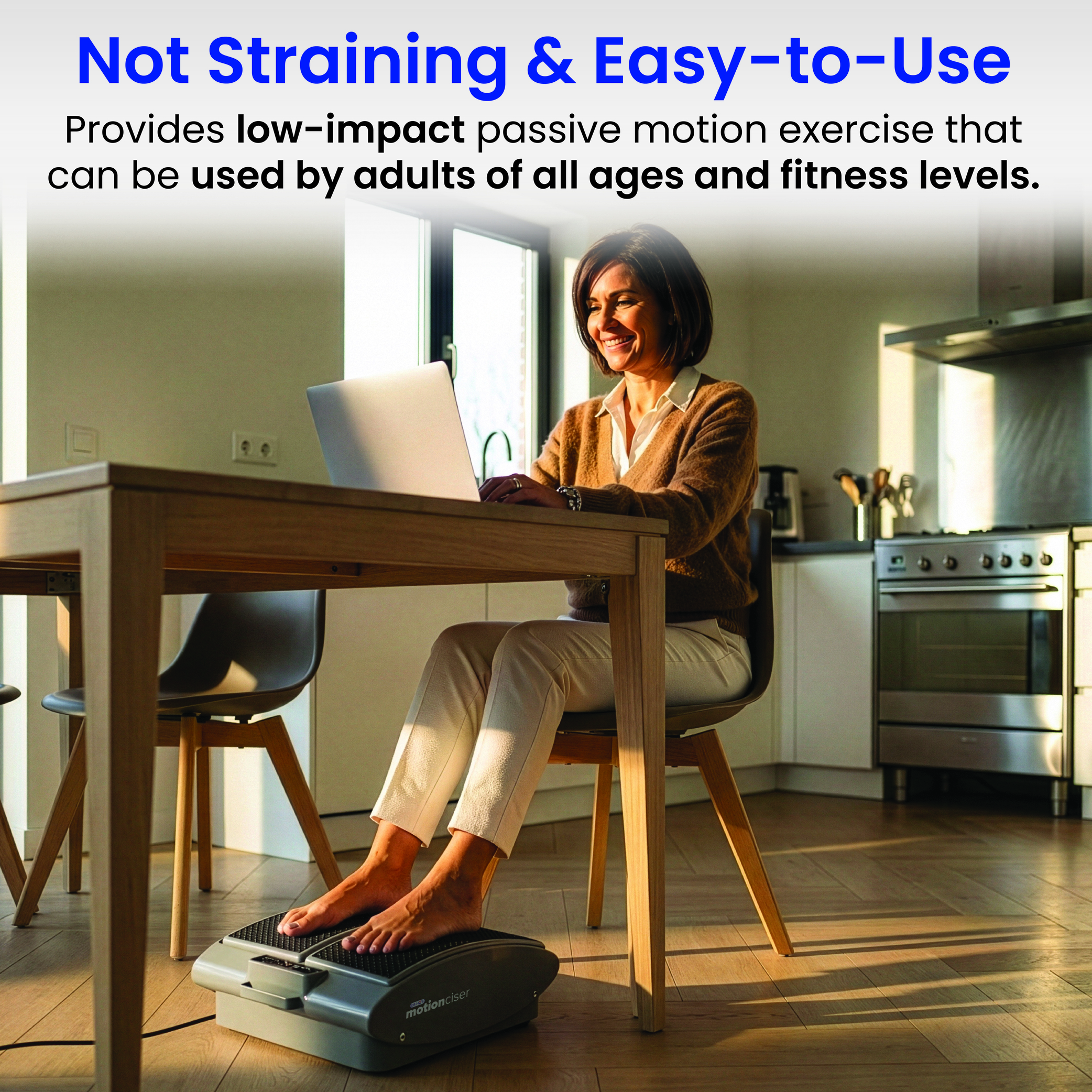 A woman uses a laptop at a table while her feet rest on a passive leg exercise machine.