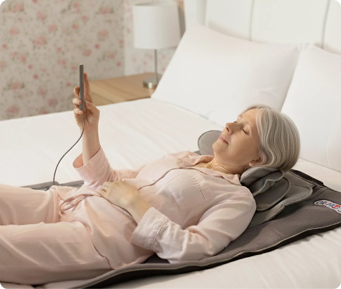 Woman lying on a bed using a heated massager with remote control.