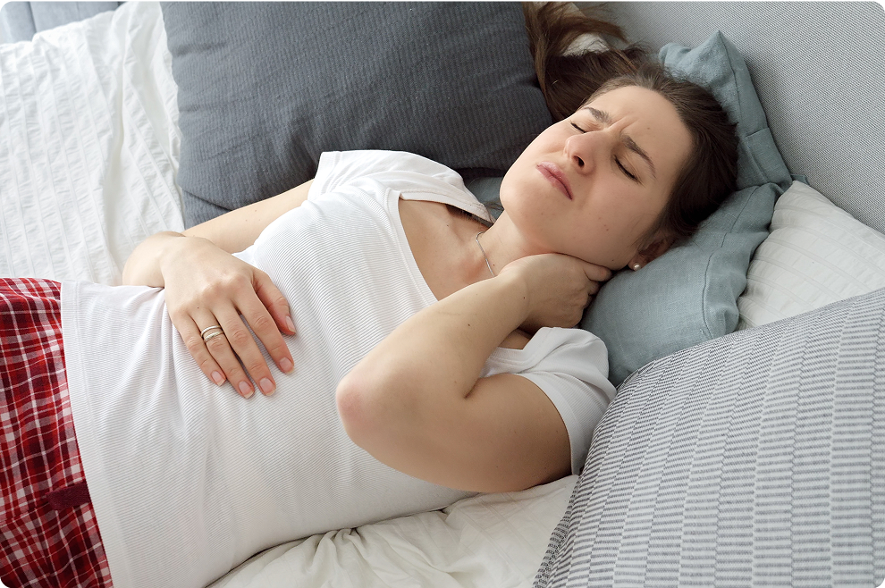 Woman lying in bed, holding her neck in discomfort.