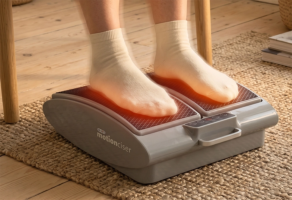 A person's feet in white socks resting on a heated motionciser foot and leg exerciser.