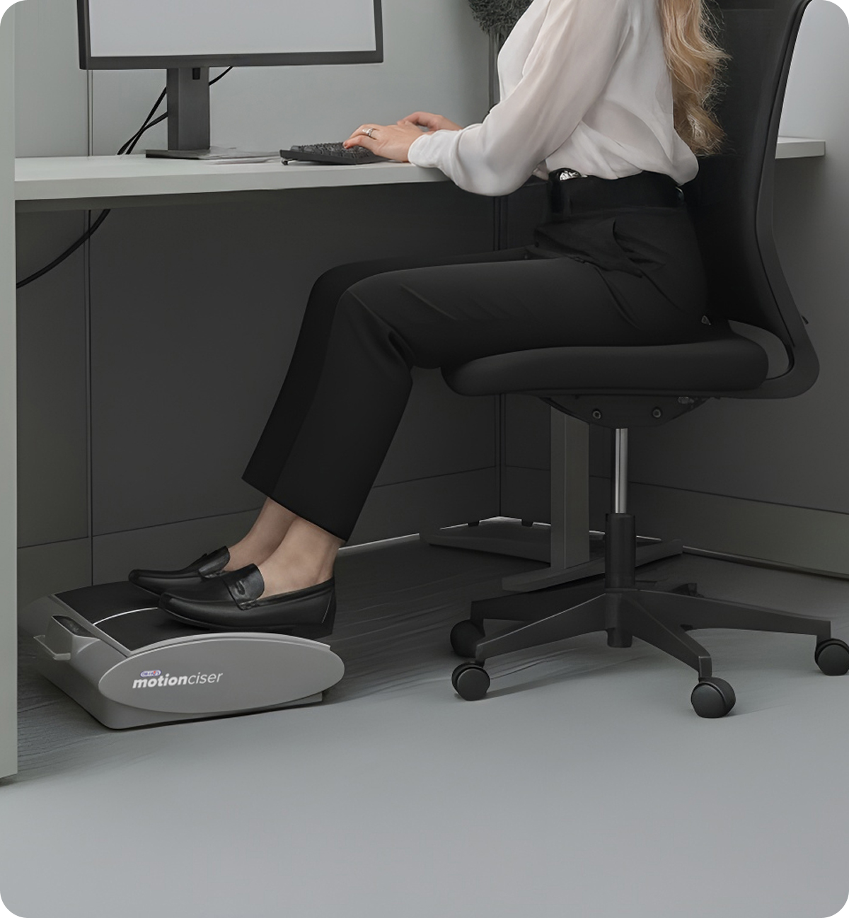 Person using a foot exercise machine under a desk in an office.