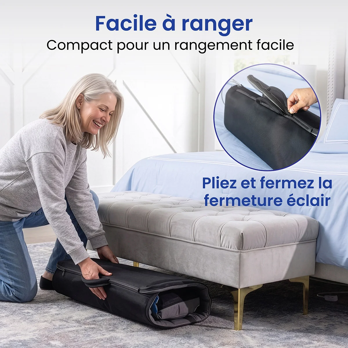 A woman puts a rolled-up mattress into a black zippered storage bag in a bedroom.