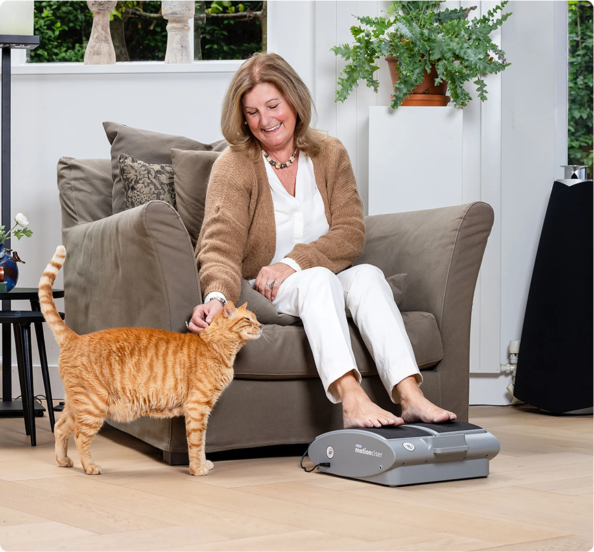 Woman sitting on a couch petting an orange cat, with feet on a foot massager.
