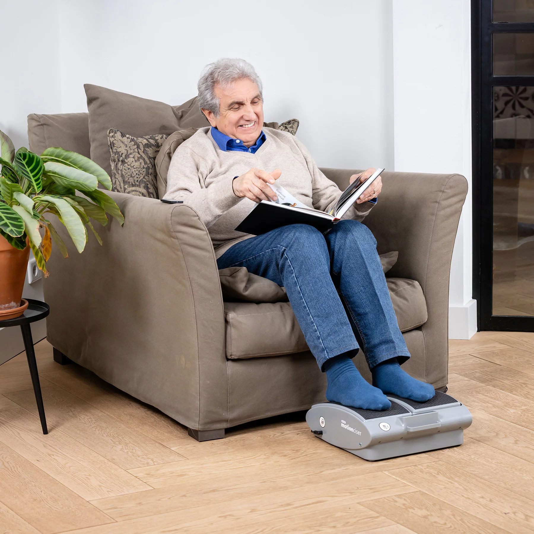 Elderly man reading a book while using a foot massager.