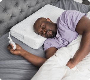 Man sleeping in bed holding a small fan.
