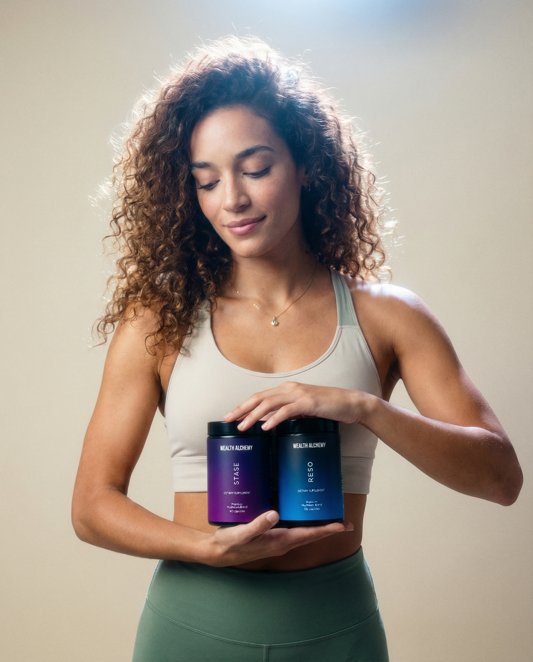 A woman in athletic wear holds two jars of Wealth Alchemy supplements while looking down at them.