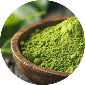 A close-up of a wooden bowl filled with vibrant green powder, with out-of-focus leaves in the background.