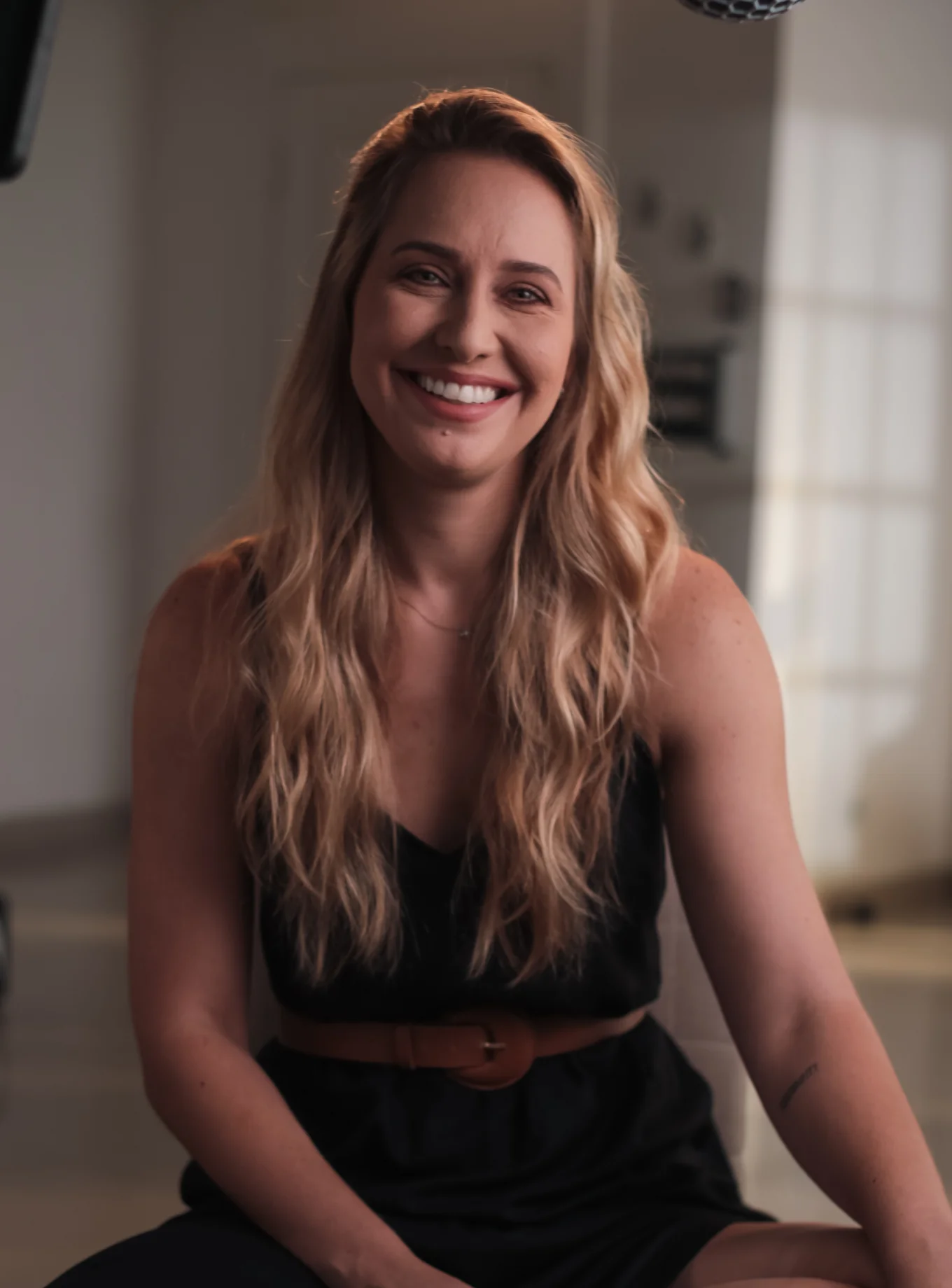 Smiling person with long blonde hair sitting indoors.
