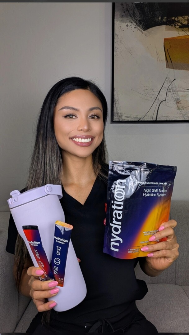 A smiling woman holds a shaker bottle and packets of 'Night Shift Nurse' hydration drink mix.