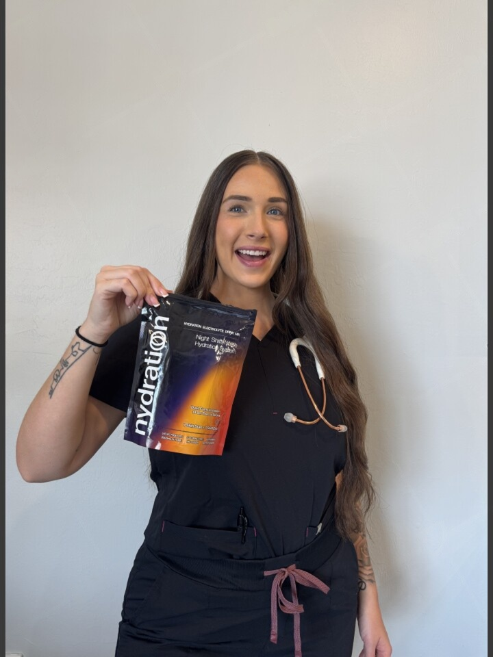 A smiling woman in black scrubs with a stethoscope holds up a packet of Nydration drink mix.
