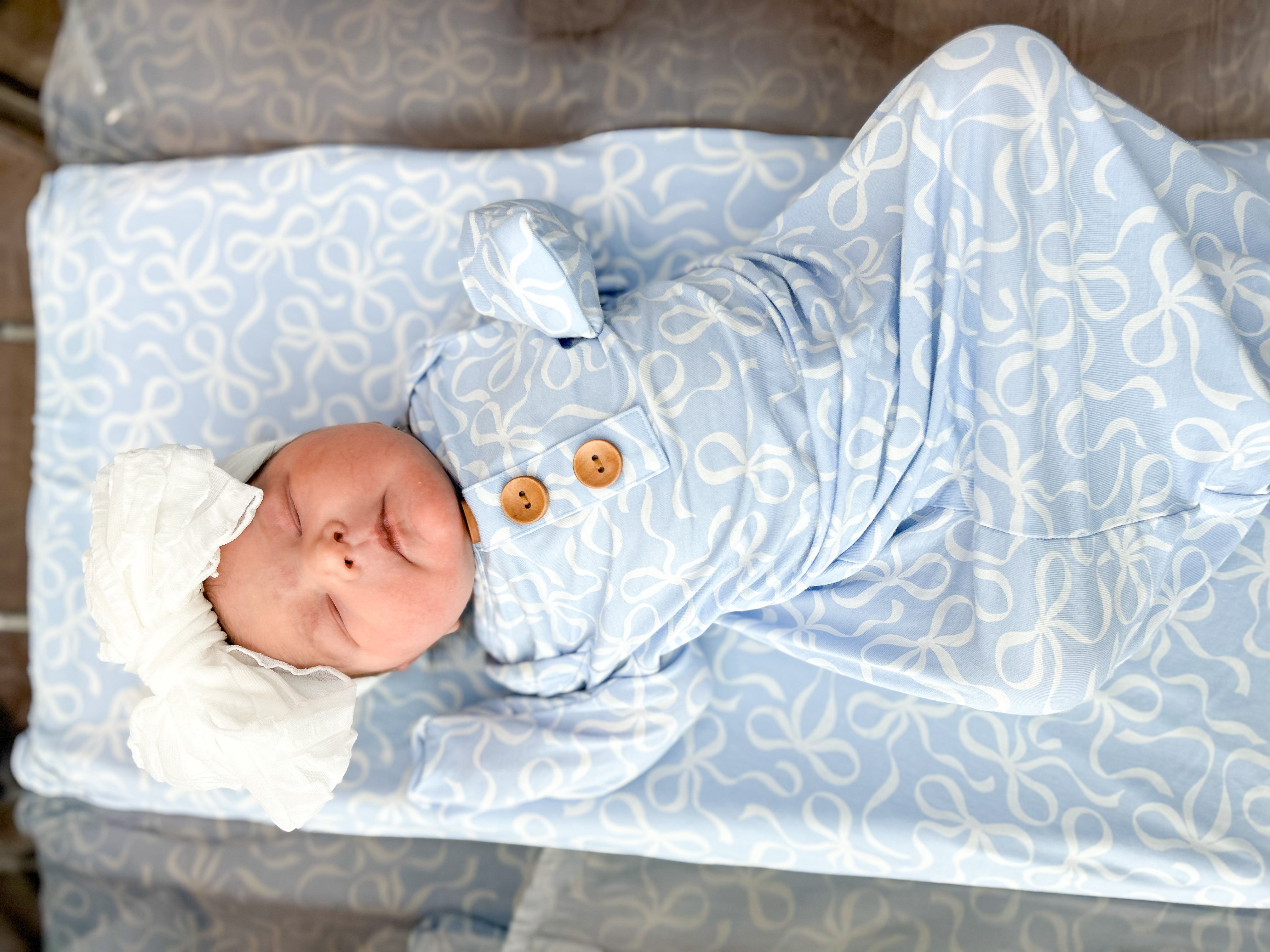 Newborn baby swaddled in blue patterned fabric with a white bow on head.