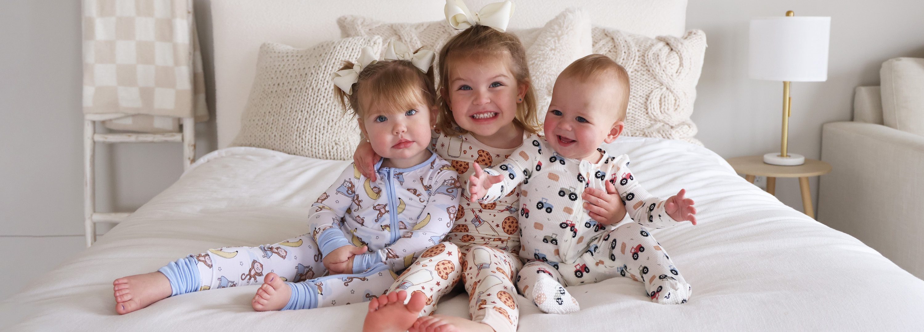 Three children in pajamas sitting on a bed, smiling.