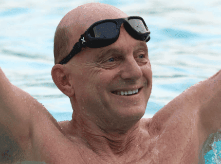 Smiling man in a swimming pool wearing goggles on his forehead.