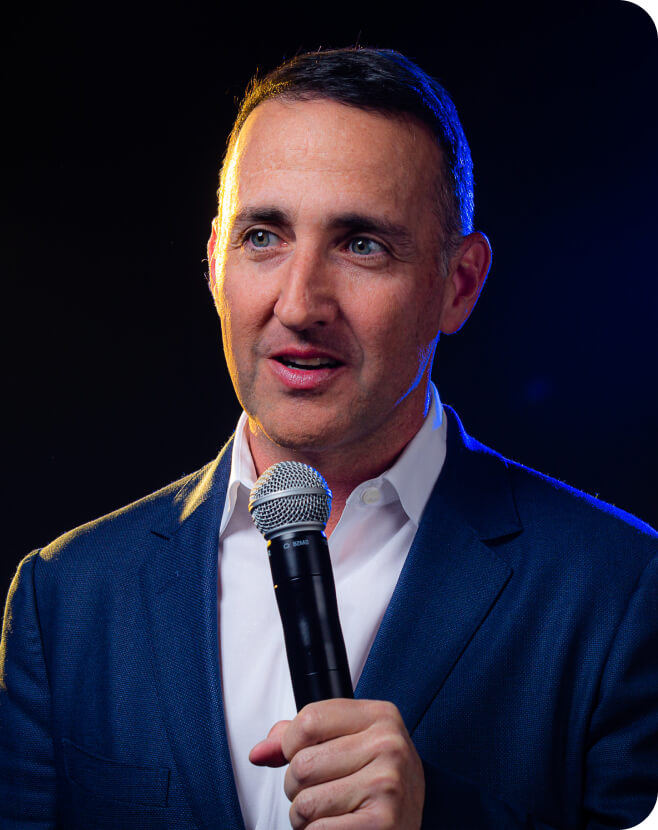 Man in blue suit holding a microphone, speaking on stage.